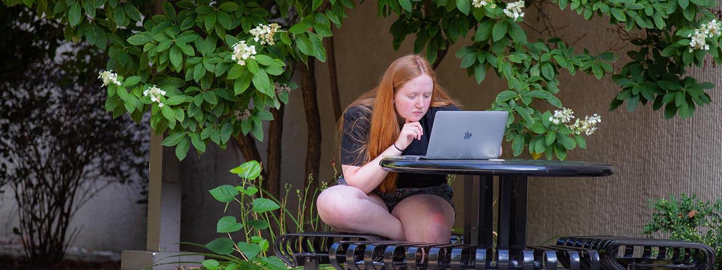一个学生坐在外面的桌子上用笔记本电脑工作.